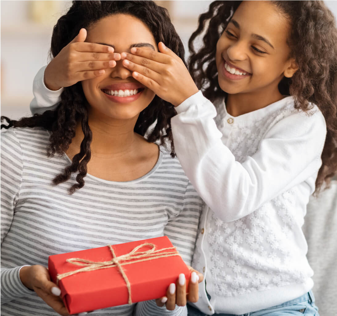 Child covering mothers eyes while giving her a gift