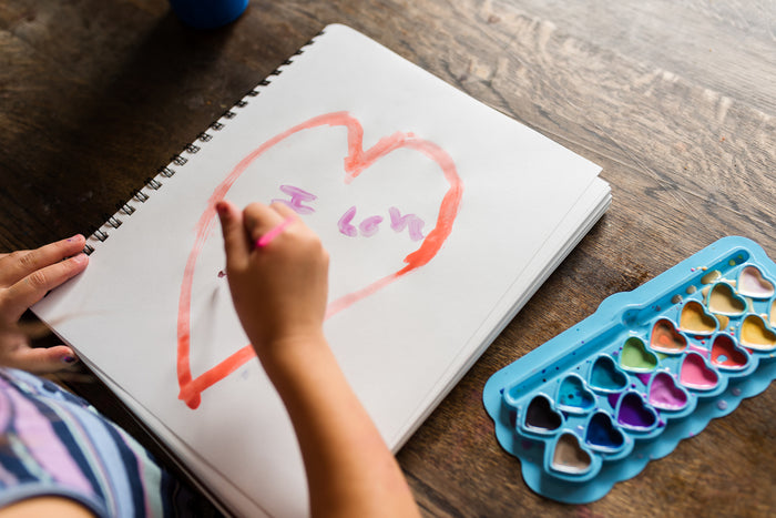 child watercoloring a heart on a notebook